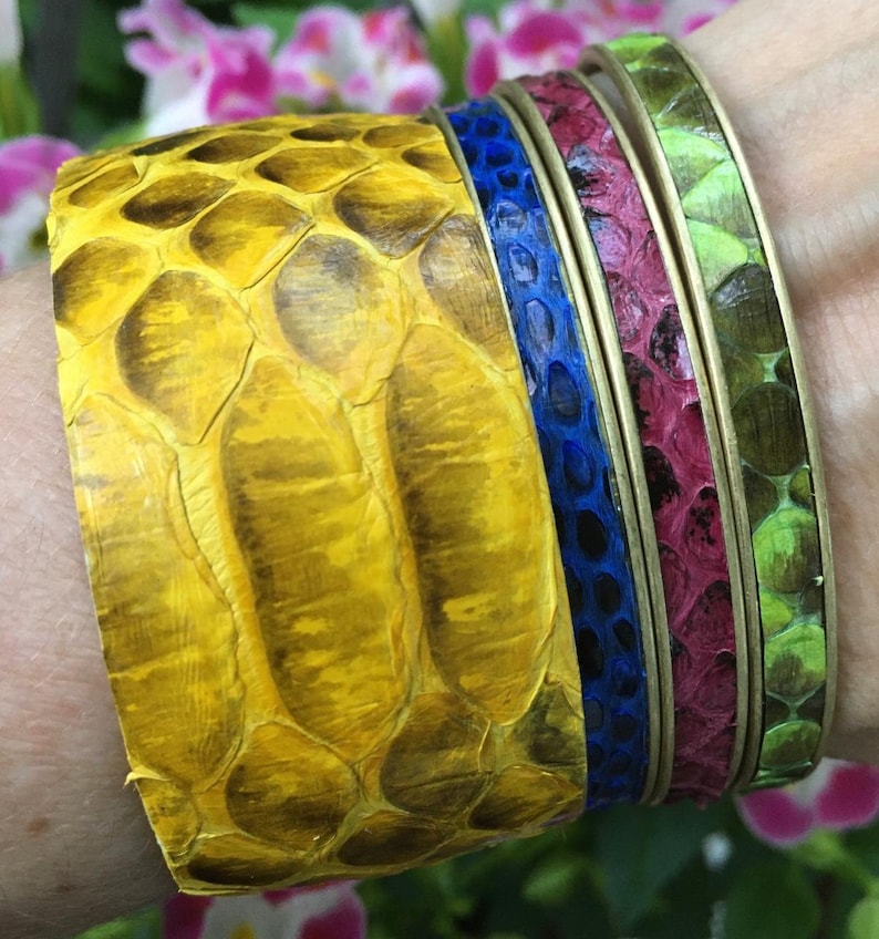 May include: A set of four colorful snake skin bracelets. The bracelets are stacked on top of each other, with the yellow bracelet on the bottom, followed by a blue bracelet, a burgundy bracelet, and a green bracelet.