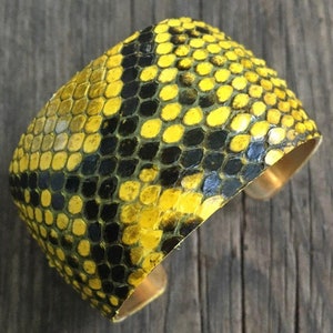 Może przedstawiać: Bransoletka z ż&oacute;łtej i czarnej sk&oacute;ry węża z mosiężnym tyłem.