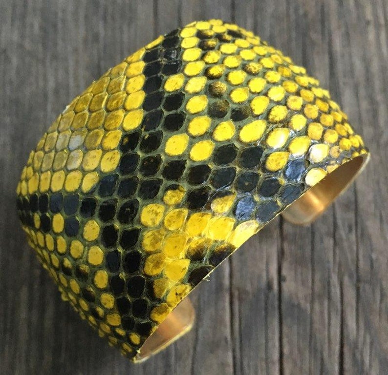 Może przedstawiać: Bransoletka z ż&oacute;łtej i czarnej sk&oacute;ry węża z mosiężnym tyłem.