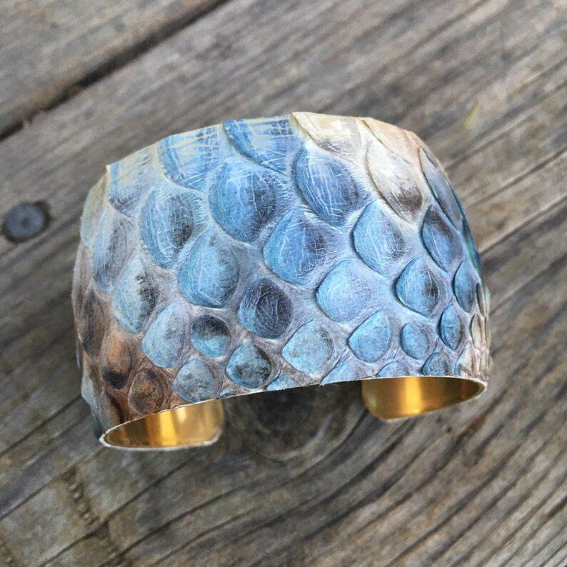 May include: A wide cuff bracelet made of blue and brown snakeskin with a gold metal band.