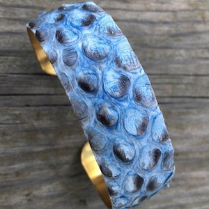 Könnte beinhalten: Ein blaues und schwarzes Schlangenleder-Armband mit Messingrücken.