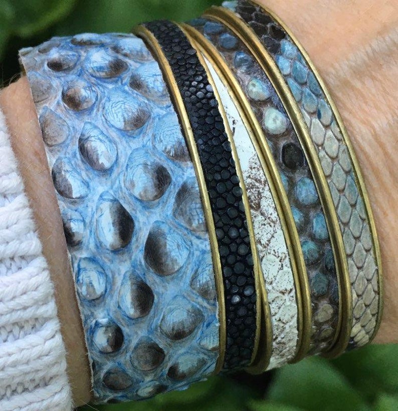 K&ouml;nnte beinhalten: Stapel von vier Lederarmb&auml;ndern mit einem blauen, wei&szlig;en und schwarzen Muster. Die Armb&auml;nder sind aus Schlangenleder und haben einen Messingbesatz.