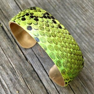 Pu&ograve; includere: Un braccialetto in pelle di serpente verde e marrone con base in rame.