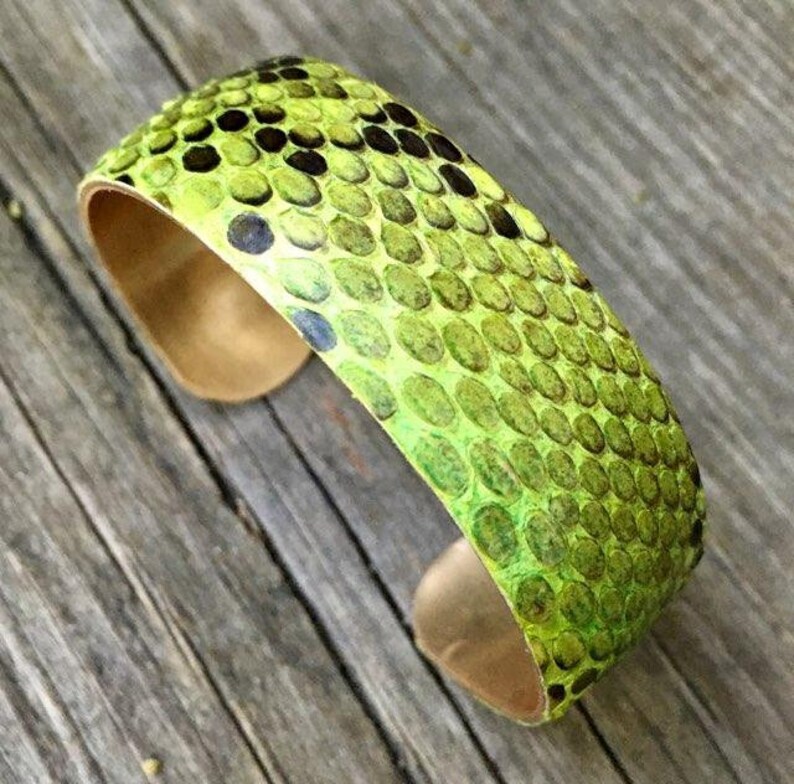 Pu&ograve; includere: Un braccialetto in pelle di serpente verde e marrone con base in rame.