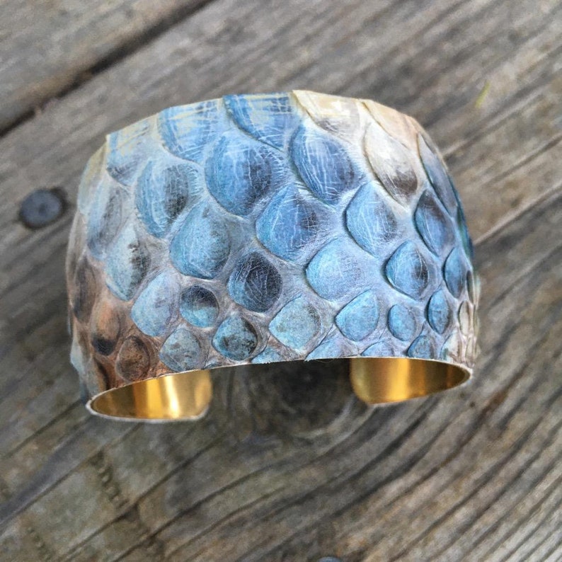 May include: A wide, gold-toned cuff bracelet with a blue and brown snakeskin pattern.