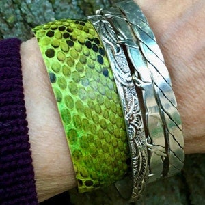 Peut inclure: Un bracelet en peau de serpent vert avec un bracelet en argent et un bracelet en argent torsadé.