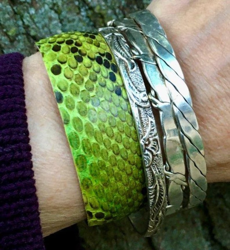 Pu&ograve; includere: Un braccialetto in pelle di serpente verde con un braccialetto in argento e un braccialetto in argento intrecciato.