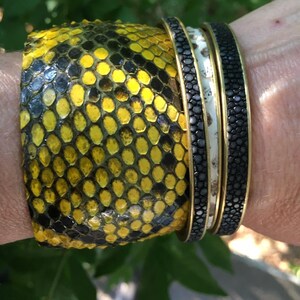 Może przedstawiać: Trzy nakładane na siebie bransoletki, jedna z wzorem sk&oacute;ry węża w kolorze ż&oacute;łtym i czarnym, druga z biało-czarnym wzorem w kropki, a trzecia z czarno-białym wzorem w kropki.