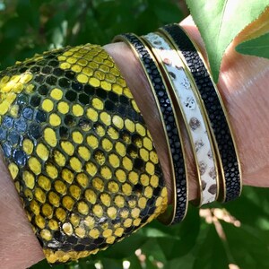 Może przedstawiać: Trzy sk&oacute;rzane bransoletki z czarno-białym wzorem. Bransoletka na dole jest ż&oacute;łta i czarna.