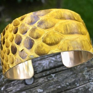 May include: A yellow snakeskin cuff bracelet with a gold metal base. The bracelet is made of real snakeskin and has a unique, textured look.
