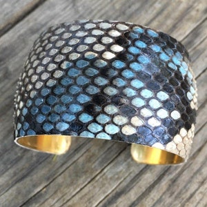 May include: A wide, blue and black snakeskin cuff bracelet with a gold metal band.