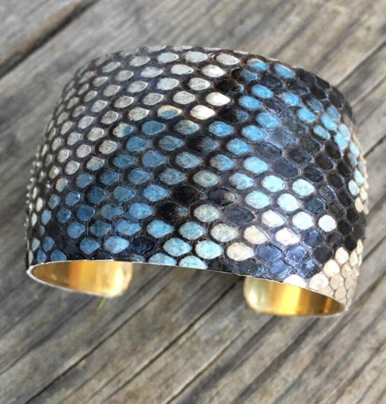 May include: A wide, blue and black snakeskin cuff bracelet with a gold metal band.