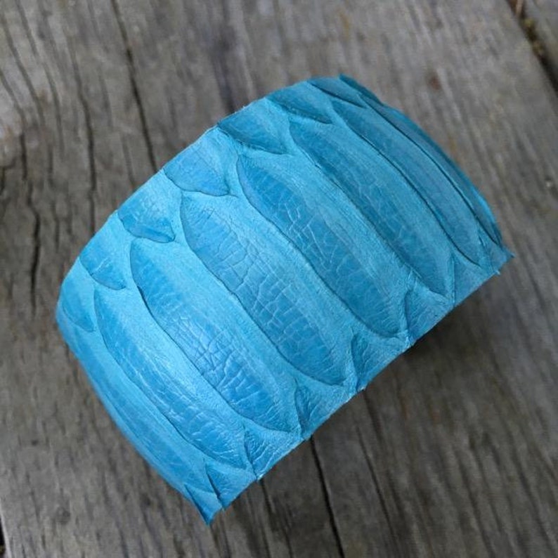 Pode incluir: Um bracelete largo de couro azul turquesa com um padr&atilde;o de folhas texturizado.