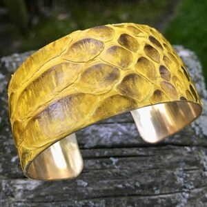 May include: A yellow snakeskin cuff bracelet with a brass base. The bracelet is made of real snakeskin and has a unique, textured look.