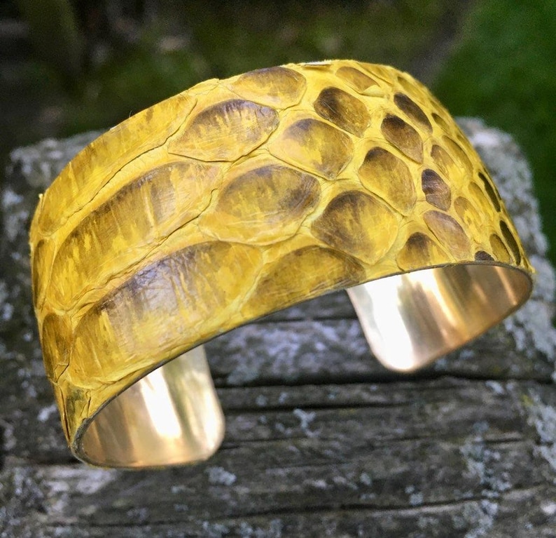 May include: A yellow snakeskin cuff bracelet with a brass base. The bracelet is made of real snakeskin and has a unique, textured look.