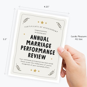 May include: A white A2 size greeting card measuring 4.25 inches by 5.5 inches. The card features black text reading Certificate of Achievement, Congratulations on passing your Annual Marriage Performance Review, and additional text, with gold stars and leaf accents.