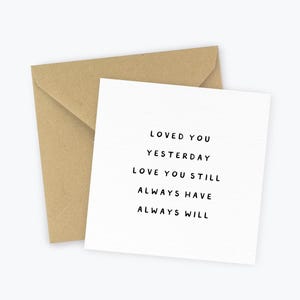May include: A white greeting card with the text "LOVED YOU YESTERDAY LOVE YOU STILL ALWAYS HAVE ALWAYS WILL" is next to a brown envelope. The card and envelope are on a white background.