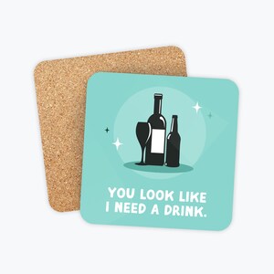 May include: A blue and white coaster with a black silhouette of a wine glass, bottle of wine, and bottle of beer. The text "You look like I need a drink." is printed on the coaster.