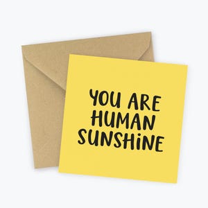 May include: A yellow card with black text that reads "You are human sunshine". The card is on a brown envelope.