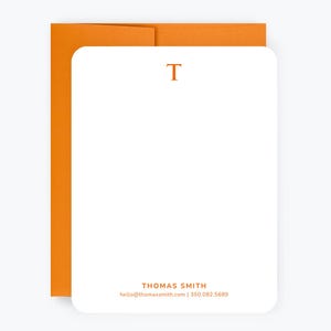 May include: A white stationery card with an orange letter "T" at the top and the text "THOMAS SMITH" and contact information at the bottom.