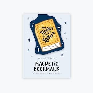 May include: A yellow book with the text "The Book is always Better" on a dark blue background with stars. The text "KREATE PAPER CO. MAGNETIC BOOKMARK © Kreate Paper Co. Made in the USA" is at the bottom of the image.