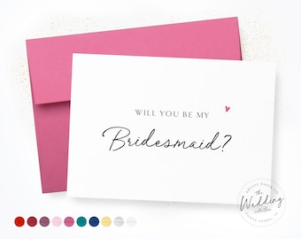 May include: A white card with the text "WILL YOU BE MY Bridesmaid?" in black script, with a small pink heart. The card is paired with a pink envelope. The Wedding Collection logo is in the bottom right corner.