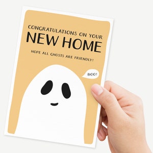 May include: A light orange card with the text "Congratulations on your new home. Hope all ghosts are friendly!" and a white ghost with black eyes and a mouth saying "Boo!"