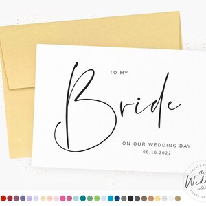 May include: A white card with black calligraphy that says "To My Bride" and "On Our Wedding Day 08.16.2022". The card is on a gold envelope.