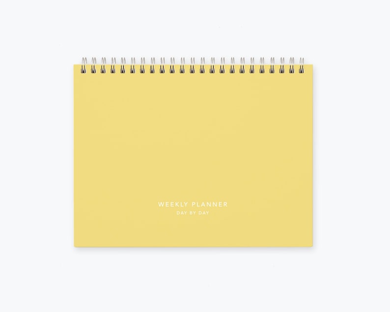 May include: A yellow weekly planner with a spiral binding and the text "WEEKLY PLANNER DAY BY DAY" printed on the front.
