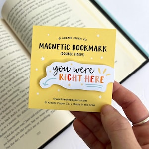 May include: Yellow magnetic bookmark with the text "you were right here" in colorful lettering. The bookmark is double-sided and features a white background with stars and a sun.