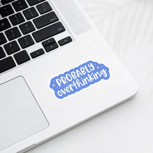 Puede incluir: Una pegatina con la frase "PROBABLY overthinking" en blanco sobre un fondo azul en forma de nube. La pegatina est&aacute; colocada sobre un ordenador port&aacute;til blanco.