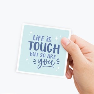 May include: A light blue card with the text "Life is tough but so are you" in a blue font with white stars and hearts.