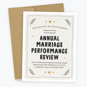 May include: A white greeting card with a brown envelope featuring the text Certificate of Achievement, Congratulations on passing your Annual Marriage Performance Review, and Your continued participation has been noted. Please accept this folded piece of card in recognition of your sustained effort, decorated with gold stars and leaf motifs.