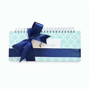 K&ouml;nnte beinhalten: Ein blau-wei&szlig;er Planer mit einem blauen Band darum gebunden. Der Planer hat ein geometrisches Muster und steht auf der Vorderseite "list it planner".