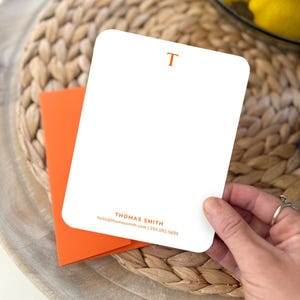 May include: A white card with an orange letter "T" at the top. The card has the text "THOMAS SMITH" and contact information at the bottom.