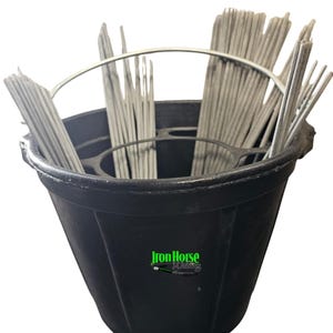 May include: A black bucket filled with gray welding rods. The bucket has a metal handle and the words "Iron Horse Welding" in green and white on the side. The rods are arranged in bundles.