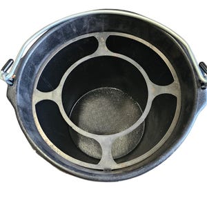May include: A black bucket with a metal handle and a silver-colored metal insert. The insert has a circular design with a series of curved supports. The bucket is viewed from above.
