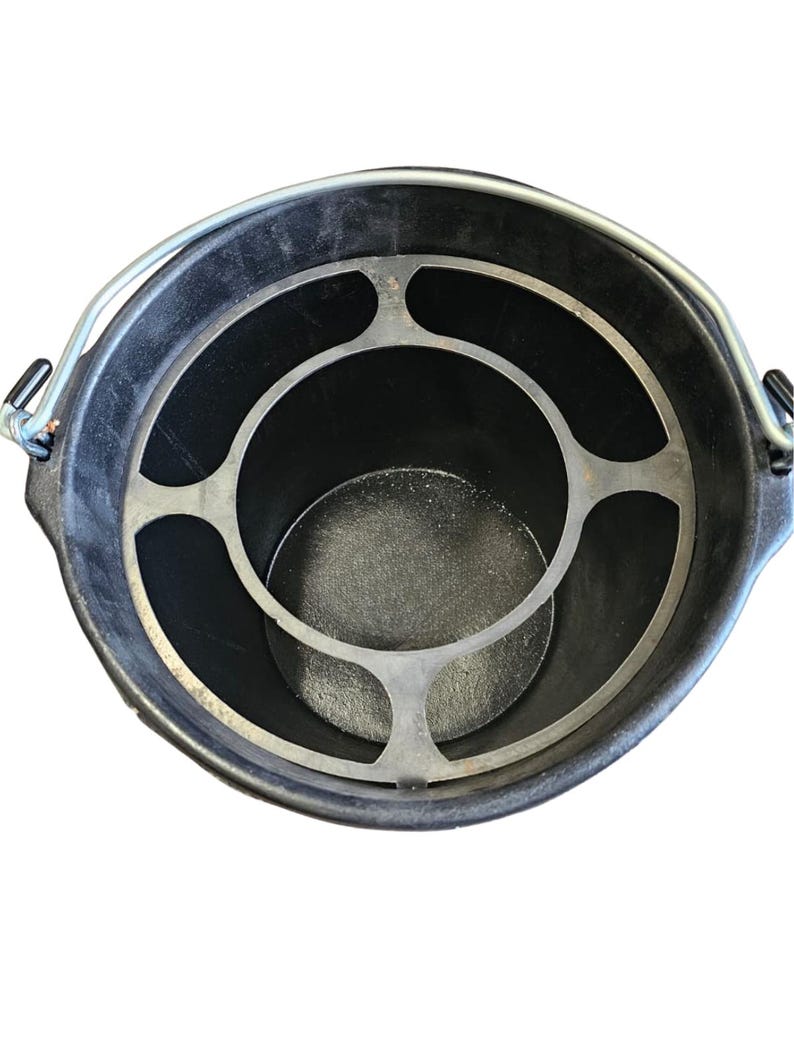 May include: A black bucket with a metal handle and a silver-colored metal insert. The insert has a circular design with a series of curved supports. The bucket is viewed from above.