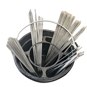 May include: A black metal bucket filled with numerous gray welding rods. The rods are arranged in bundles and held in place by a metal frame. The image is taken from a high angle, showing the contents of the bucket.