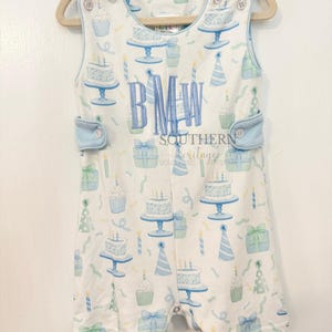 May include: A white sleeveless romper with a blue and green birthday cake and cupcake pattern. The romper has a blue trim and buttons. The romper has the monogram "BMW" embroidered on the front. The romper is made by Southern Heritage.