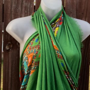 May include: A bright green scarf with a geometric pattern in orange, blue, yellow, and red. The scarf is draped over a mannequin. The design is visible on the edges of the scarf, adding a splash of colour to the green fabric.
