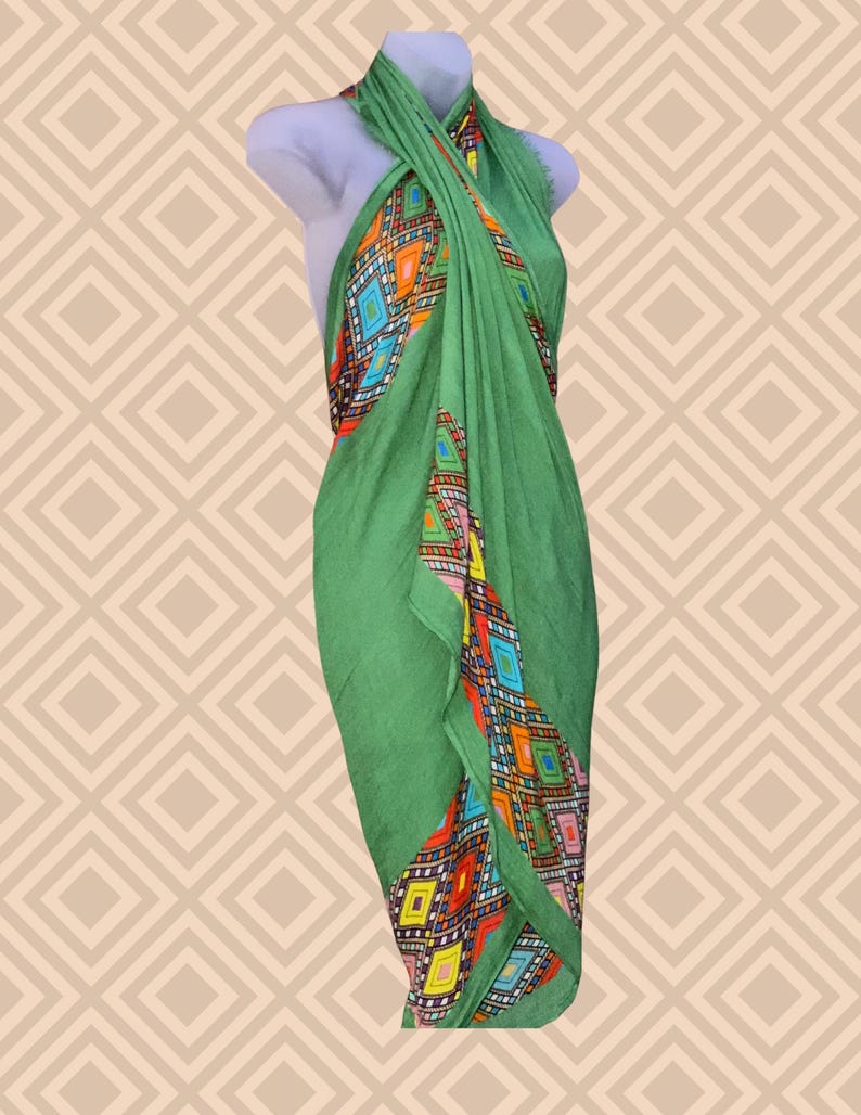 May include: A green sarong with a colourful geometric pattern. The sarong is draped over a mannequin, showcasing its design. The pattern features diamonds in shades of orange, blue, yellow, and red. The fabric appears lightweight and suitable for warm weather.