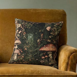 May include: A square throw pillow featuring a dark forest scene with various mushrooms and foliage in shades of green, brown, and cream, placed on a mustard yellow upholstered armchair with rounded arms and a thick seat cushion.