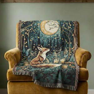 May include: A woven throw blanket featuring a detailed illustration of a fox sitting in a dark forest at night. The scene includes a large crescent moon, glowing fireflies, and dense foliage in shades of deep green, brown, and golden yellow.