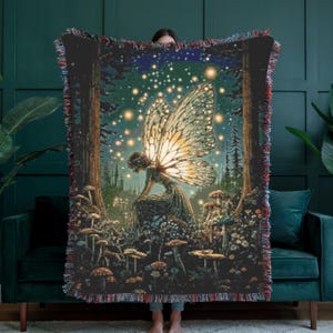 May include: A woven tapestry throw blanket featuring a fairy in a forest scene with mushrooms and glowing lights. The artwork has a dark color palette with a fringed edge. The fairy has large, detailed wings.
