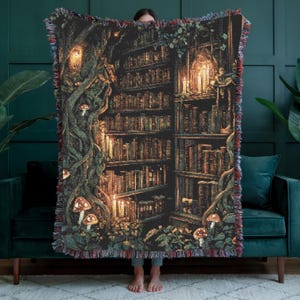 Könnte beinhalten: Eine gewebte Decke mit einer detaillierten Illustration einer Bibliotheksszene. Das Design umfasst Bücherregale voller Bücher, leuchtende Kerzen und skurrile Pilzakzente. Die Farbpalette wird von warmen Brauntönen, Grüntönen und roten Akzenten dominiert.