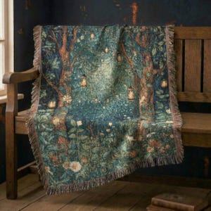 May include: A woven throw blanket featuring a dark teal and green forest scene with tall trees, hanging lanterns, and scattered white flowers. The blanket has a textured, tapestry-style weave and a fringed edge along the top and bottom borders.