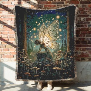 May include: A woven throw blanket featuring a fairy in a forest scene with mushrooms and glowing lights. The fairy has large, detailed wings. The color palette includes greens, browns, and blues, creating a whimsical and enchanting design.