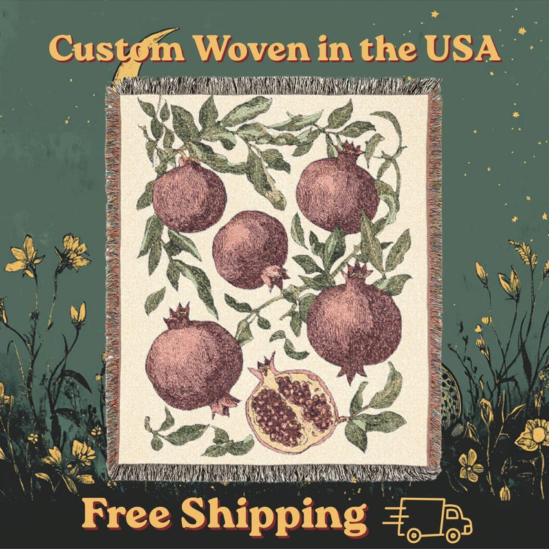 May include: A rectangular woven throw blanket featuring a cream-colored background with a botanical pattern of dark red pomegranates and green leaves. The blanket has fringed edges on the top and bottom. The text Custom Woven in the USA is visible.