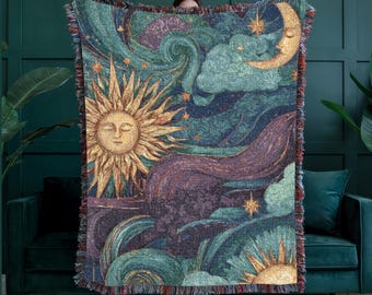 May include: A woven tapestry blanket featuring a celestial design with a sun, moon, stars, and swirling clouds in shades of gold, teal, purple, and blue. The blanket has a fringed edge.